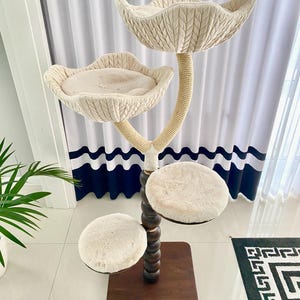 Pode incluir: Uma &aacute;rvore para gatos bege com uma base de madeira e um poste coberto de corda. A &aacute;rvore tem tr&ecirc;s plataformas, duas das quais t&ecirc;m a forma de p&eacute;talas de flores e s&atilde;o cobertas com um tecido macio bege. A terceira plataforma &eacute; redonda e &eacute; coberta com um tecido macio e felpudo bege.