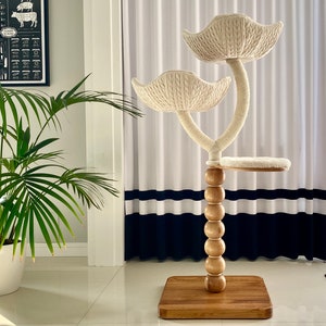 May include: A white cat tree with two platforms and a base made of wood. The platforms are covered in a soft, white fabric. The base is a dark brown wood with a round, wooden post in the center. The post is decorated with a series of wooden beads.