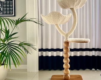 May include: A white cat tree with two platforms and a base made of wood. The platforms are covered in a soft, white fabric. The base is a dark brown wood with a round, wooden post in the center. The post is decorated with a series of wooden beads.