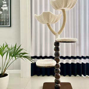 Pode incluir: Uma &aacute;rvore para gatos com uma base de madeira marrom e um poste alto de madeira marrom com uma s&eacute;rie de contas de madeira marrom. O poste &eacute; coroado com tr&ecirc;s plataformas brancas e felpudas com forma de p&eacute;talas de flores. As plataformas s&atilde;o conectadas por uma corda bege.
