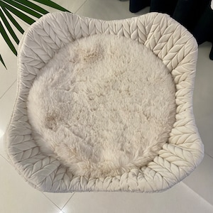 Pode incluir: Uma cama redonda e fofa para animais de estima&ccedil;&atilde;o de cor branca com uma borda acolchoada em forma de folha branca.