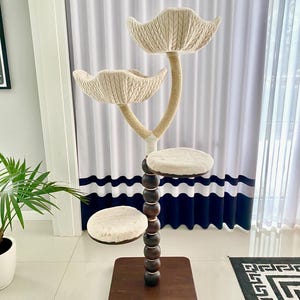 Pode incluir: Uma &aacute;rvore para gatos bege com tr&ecirc;s plataformas e um poste alto marrom com contas de madeira. As plataformas s&atilde;o cobertas com tecido macio bege e o poste &eacute; envolto em corda de sisal. A &aacute;rvore para gatos est&aacute; sobre uma base de madeira marrom.