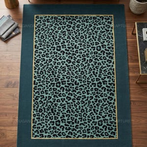 May include: Teal rectangular area rug with a leopard print center and a teal border. The leopard print features black spots on a light teal background, framed by a thin gold border. The rug is placed on a wooden floor.
