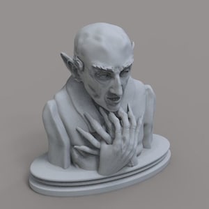 May include: A gray bust of a vampire with sharp features, long fingers, and pointed ears. The sculpture is set on a tiered, oval base. The vampire's expression is intense, with a furrowed brow and open mouth.