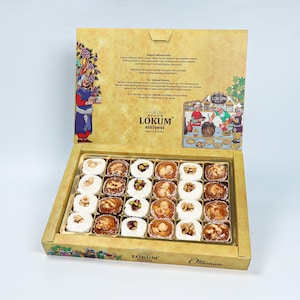 Può includere: Una scatola aperta di delizie turche, un dolce tradizionale, con vari condimenti come noci e pistacchi. La scatola è color oro con illustrazioni e testo, tra cui il marchio "Afyon Lokum Atölyesi".