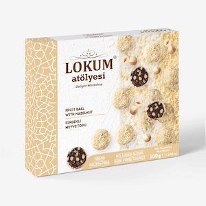 May include: A box of Lokum Atölyesi fruit balls with hazelnuts. The box is white with gold accents and text. The fruit balls are coated in a white powder and some have a dark center. The box states "Vegan" and "Gluten Free".