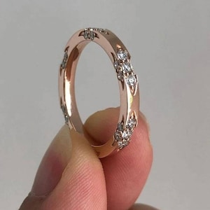 Puede incluir: Un anillo de banda de oro rosa con una fila de pequeños diamantes engastados en la banda.
