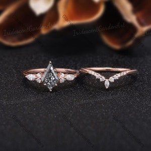 Puede incluir: Un anillo de compromiso de oro rosa con un diamante negro en forma de pera y una banda de boda de oro rosa a juego con una fila de pequeños diamantes en forma de V.