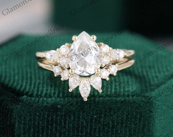 May include: A pear-shaped diamond engagement ring set with a halo of smaller diamonds. The ring is set in yellow gold and has a delicate band.