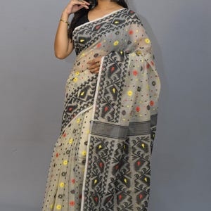 May include: A white and black patterned saree with red and yellow accents. The saree is made of a lightweight fabric and has a delicate floral design.