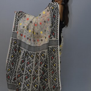 May include: A white and black patterned saree with red and yellow accents. The saree is made of a sheer fabric and has a floral design.