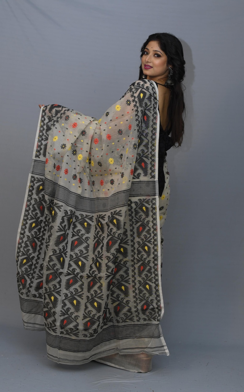 May include: A white and black patterned saree with red and yellow accents. The saree is made of a sheer fabric and has a floral design.