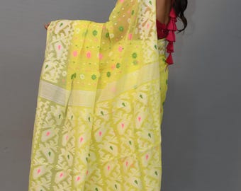 May include: A woman wearing a yellow saree with a white floral pattern and a white border. The saree has pink and green accents. The woman is wearing a red top with pink tassels.