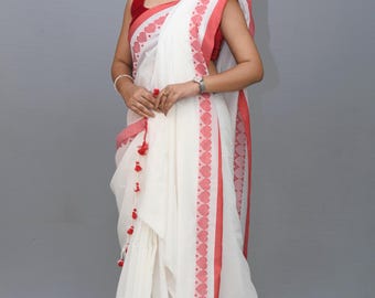May include: A white saree with a red border and heart-shaped design. The saree has a red and white tassel on the end.