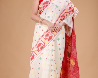May include: A white saree with a red border and accents. The saree features a repeating pattern of colorful dots and geometric shapes. The red border has a detailed design. The saree is draped over a person.