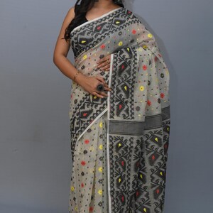 May include: A white saree with black and red geometric patterns. The saree is sheer and has a floral design. The saree is draped on a woman.