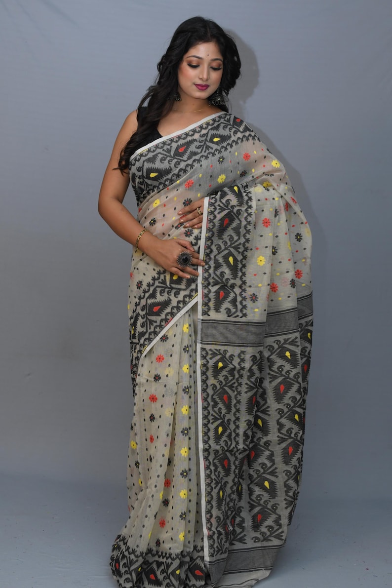 May include: A white saree with black and red geometric patterns. The saree is sheer and has a floral design. The saree is draped on a woman.