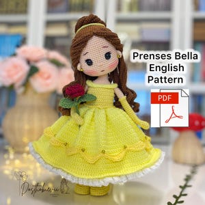 May include: A crocheted doll of a princess in a yellow dress, holding a red rose. The doll has brown hair and is wearing gold earrings. The text "Prenses Bella English Pattern" is visible on the right side of the image, along with a PDF icon.