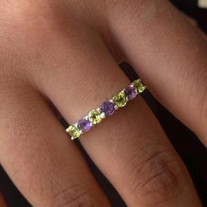 Op de afbeelding: Een zilveren ring met afwisselende paarse en groene edelstenen.