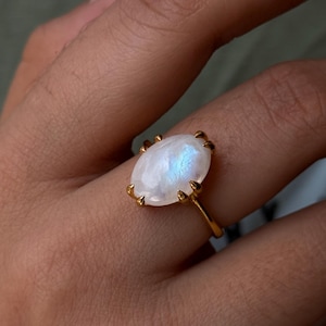 May include: A gold ring with a large oval moonstone. The stone has a white iridescent sheen.