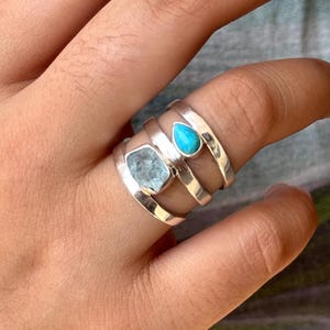 May include: A silver ring with three stacked bands, featuring a light blue aquamarine stone and a turquoise stone.