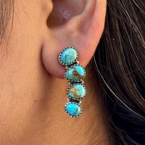 May include: A silver earring with four oval turquoise stones. Each stone is a vibrant blue-green color with brown matrix patterns. The stones are set in a scalloped silver bezel.
