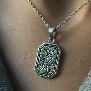 Peut inclure: Un collier en argent avec un pendentif rectangulaire orné d'un motif floral complexe.