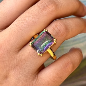 May include: A gold ring featuring a large, rectangular, iridescent gemstone. The gemstone displays shades of purple, green, and blue.