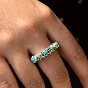 Op de afbeelding: Een zilveren ring met turquoise stenen in een stervormig ontwerp.