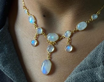 May include: A gold necklace with a teardrop pendant featuring multiple oval-shaped moonstone gems.
