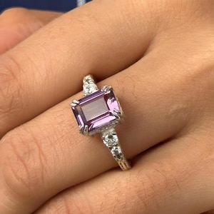 May include: A silver ring with a large, rectangular, purple gemstone surrounded by smaller, clear gemstones.