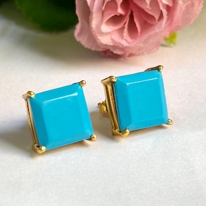 May include: A pair of gold square earrings with turquoise blue stones.