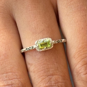 Könnte beinhalten: Ein silberner Ring mit einem grünen Edelstein, der in einem filigranen Design gefasst ist.