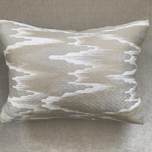 May include: Rectangular decorative pillow with a neutral color palette. The pillow features a textured pattern in shades of beige, gray, and white, creating a subtle, abstract design. The pillow is designed for home decor.