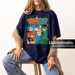 Puede incluir: Una camiseta azul marino de manga corta con un estampado gr&aacute;fico de personajes de anime de YuYu Hakusho. El dise&ntilde;o incluye un personaje central se&ntilde;alando hacia adelante, rodeado de paneles m&aacute;s peque&ntilde;os de otros personajes y texto japon&eacute;s en naranja y azul.