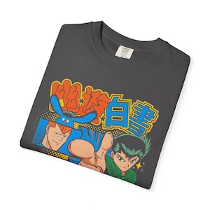 Puede incluir: Una camiseta gris carb&oacute;n con un estampado gr&aacute;fico de dos personajes de anime y una criatura azul. El dise&ntilde;o incluye texto en japon&eacute;s naranja y azul en la parte superior, con un estilo de c&oacute;mic que muestra a un personaje se&ntilde;alando al frente.