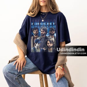 Puede incluir: Una camiseta azul marino con un gr&aacute;fico de estilo vintage del elenco del programa de televisi&oacute;n "The Goldbergs" con el texto "Goldberg Joe" impreso en la parte delantera.