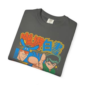 Puede incluir: Una camiseta gris carb&oacute;n con un estampado gr&aacute;fico de dos personajes de anime, uno con cabello rojo y otro con cabello verde oscuro, junto a una criatura azul. El dise&ntilde;o incluye texto japon&eacute;s en naranja y azul brillante.