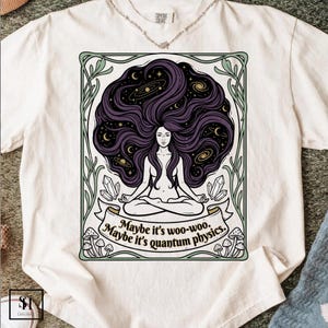 Puede incluir: Camiseta blanca con un gráfico de una mujer meditando con cabello morado largo lleno de galaxias y estrellas. El diseño incluye el texto "Maybe it's woo-woo. Maybe it's quantum physics."