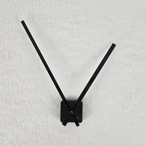 Könnte beinhalten: Schwarze Uhrzeiger mit einem quadratischen Uhrwerk vor einem weißen, flauschigen Hintergrund.