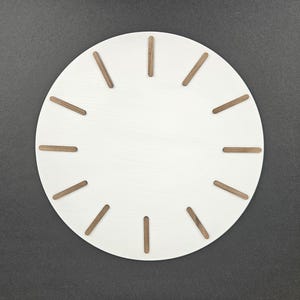Może przedstawiać: Biały, okrągły zegar ścienny z brązowymi drewnianymi znacznikami godzin. Tarcza zegara jest prosta, o minimalistycznym designie. Zegar jest umieszczony na ciemnoszarym tle.
