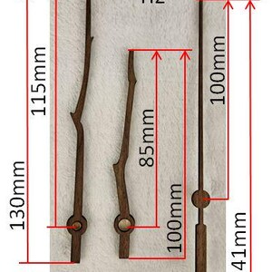 May include: Three wooden clock hands in varying styles. The longest hand is 130mm long, the second is 85mm, and the third is 141mm. The hands are dark brown and have a natural, twig-like design. The image includes measurements in millimeters.