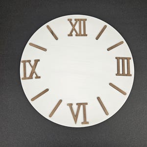 May include: A white, round clock face with Roman numerals and hour markers. The numerals and markers are a dark brown color, contrasting with the white background. The clock face is a decorative item.