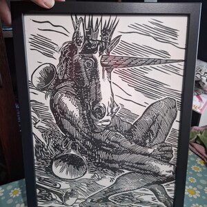 Op de afbeelding: Zwart-witte houtsnede van een mythisch wezen met een kroon en een hoorn, ingelijst in een zwart frame.