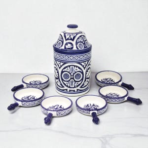 Puede incluir: Un juego de cocina de cerámica con un tarro alto con tapa y seis platos pequeños con asas. El juego es blanco con intrincados diseños azules. Los platos tienen un diámetro de aproximadamente 10 cm.