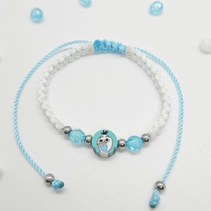 Könnte beinhalten: Ein blau-weißes Makramee-Armband mit einem Cartoon-Olaf-Charakter. Das Armband hat blaue und silberne Perlen und einen Schiebeknotenverschluss. Ein lustiges Accessoire für Fans des Films.
