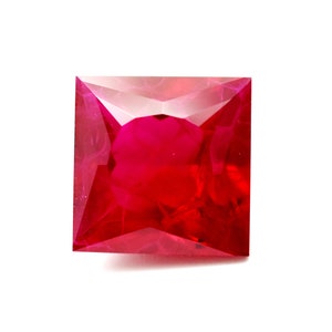 May include: Square-cut, vibrant red gemstone with a polished surface. The gem has a deep, rich color and a faceted design, reflecting light. The gemstone is set against a white background, highlighting its color and shape. This gem is suitable for jewelry.
