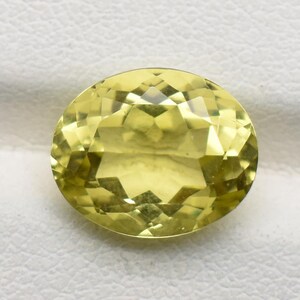 Può includere: Una gemma sfaccettata, di forma ovale e di colore giallo pallido. La gemma è tagliata per massimizzare la riflessione della luce, mostrando un aspetto brillante e scintillante. La gemma è su uno sfondo bianco.