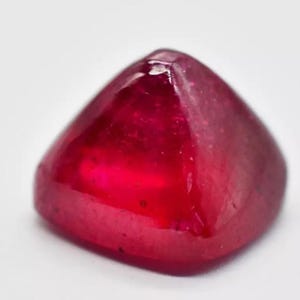 May include: A deep red gemstone with a faceted, pyramid-shaped cut. The gemstone is polished and has a glossy finish.