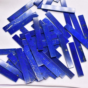 May include: A collection of rectangular, deep blue lapis lazuli gemstone pieces. The stones have a polished finish with natural gold flecks and variations in color. These pieces are ideal for jewelry making or other craft projects.